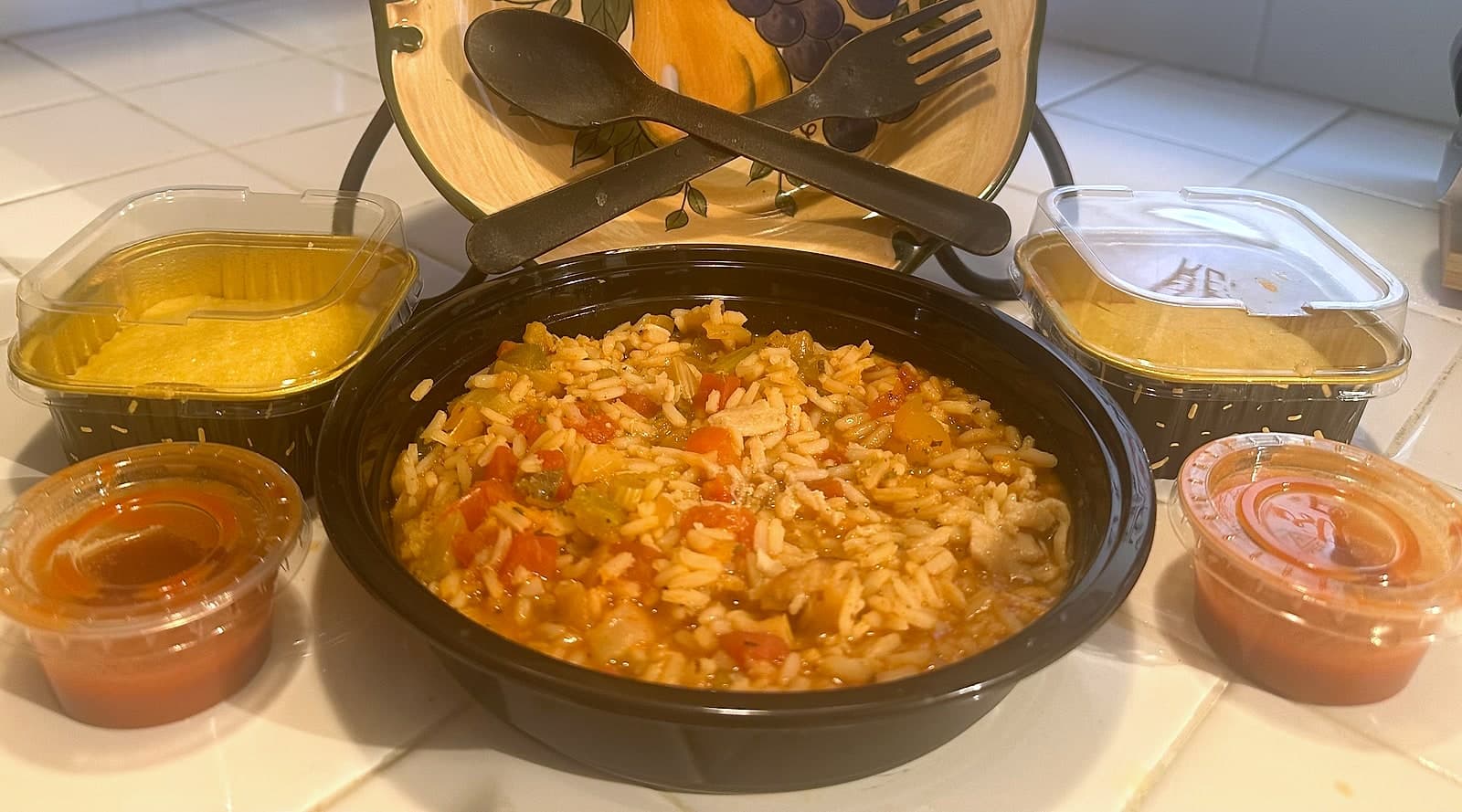 22 oz bowl of vegan jambalaya with vegetables and rice, served with cornbread and sauces